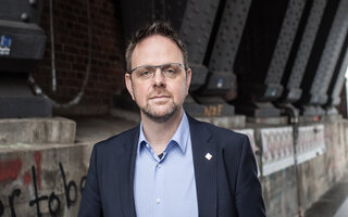 Guido Zeitler steht unter einer S-Bahn-Brücke. Er trägt einen Anzug und schaut freundlich in die Kamera.