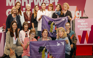 Die Mitglieder des NGG-Bundesfrauenausschusses halten zwei Fahnen der NGG-Frauen in die Kamera